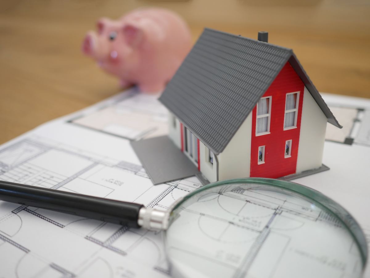 maison en jouet sur plan d'architecte avec une loupe et une tirelire cochon pour symboliser la recherche d'economie